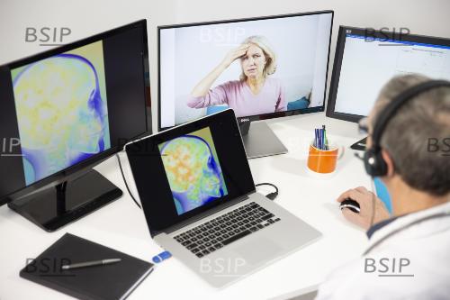 Médecin, en téléconsultation, avec une femme de 45 ans pour une douleur à la tête ; sur l'écran apparaît une radiographie de cerveau. 